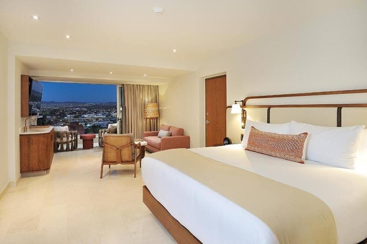 A hotel room with a large bed, a desk, a chair, and a view of a cityscape.