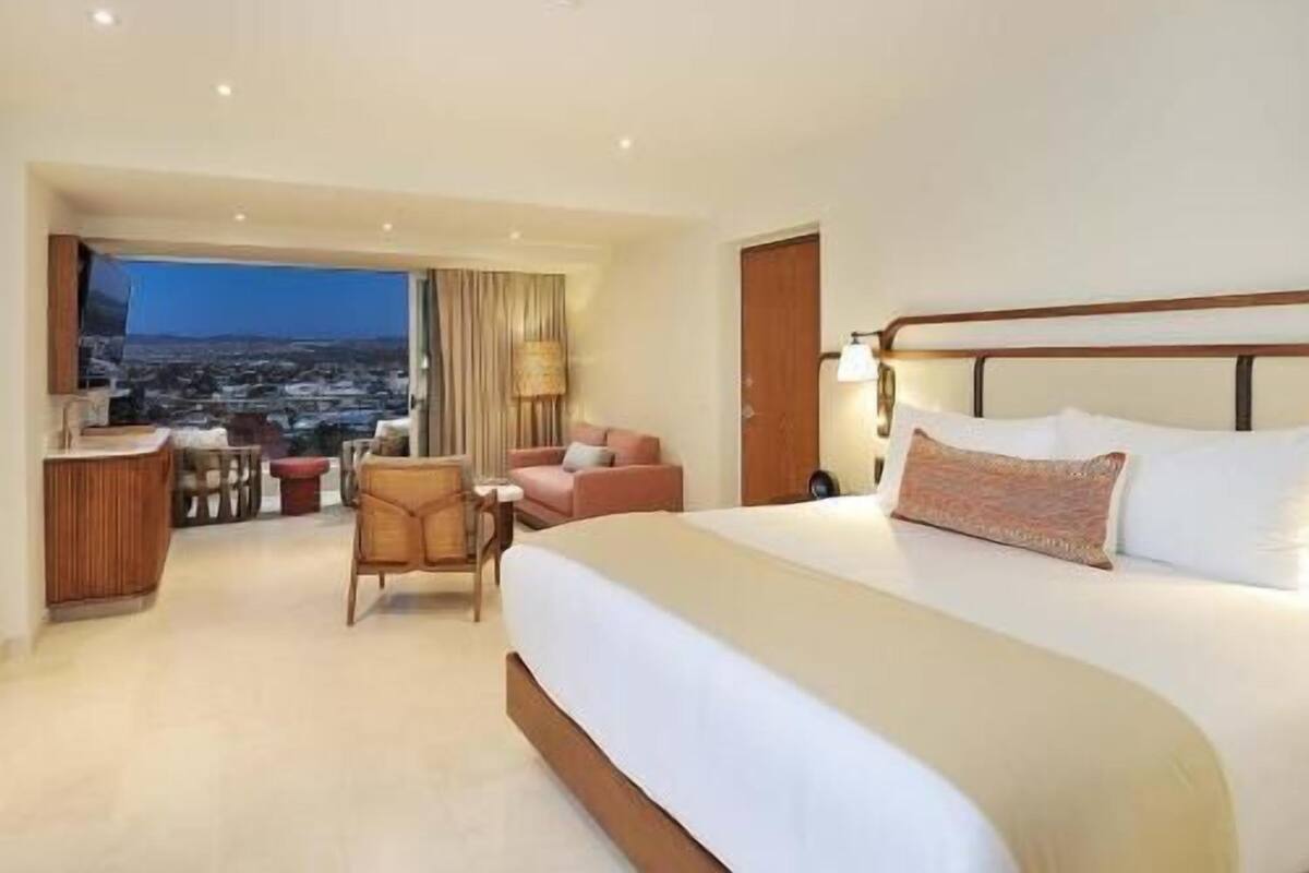 A hotel room with a large bed, a desk, a chair, and a view of the cityscape.