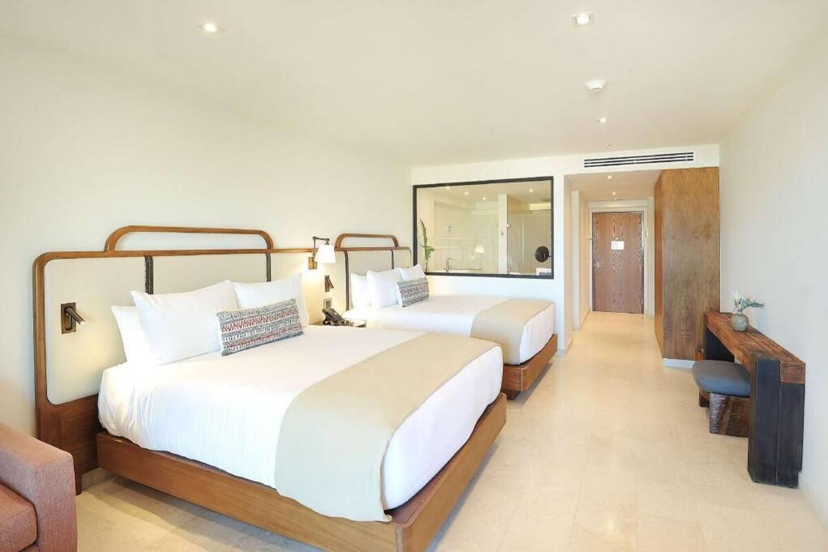 A hotel room with two beds, a desk, and a mirror.