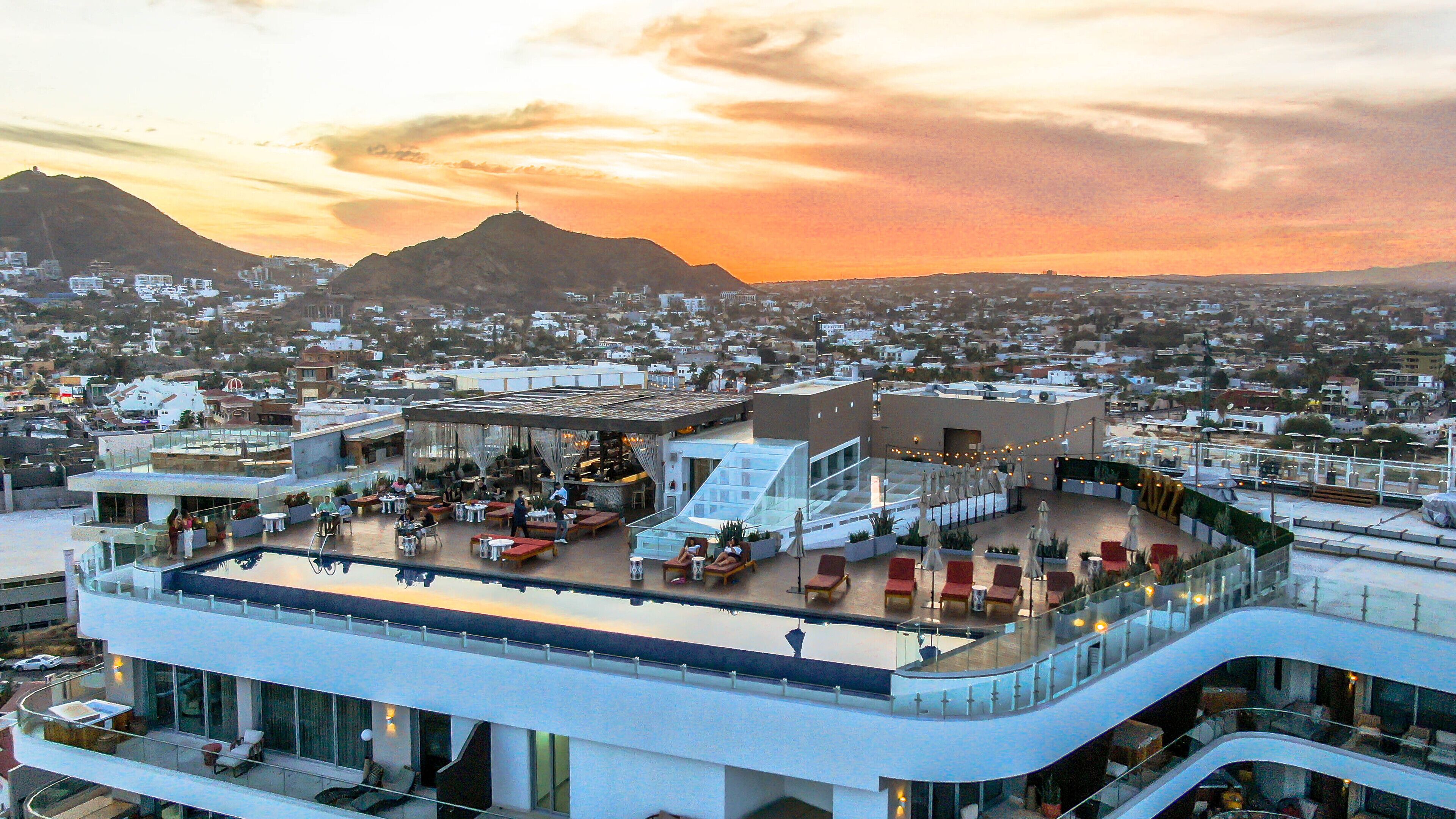 Eine Dachterrasse mit Außenbereich und einer gläsernen Lounge, mit Blick auf eine Stadtlandschaft und Berge im Hintergrund.