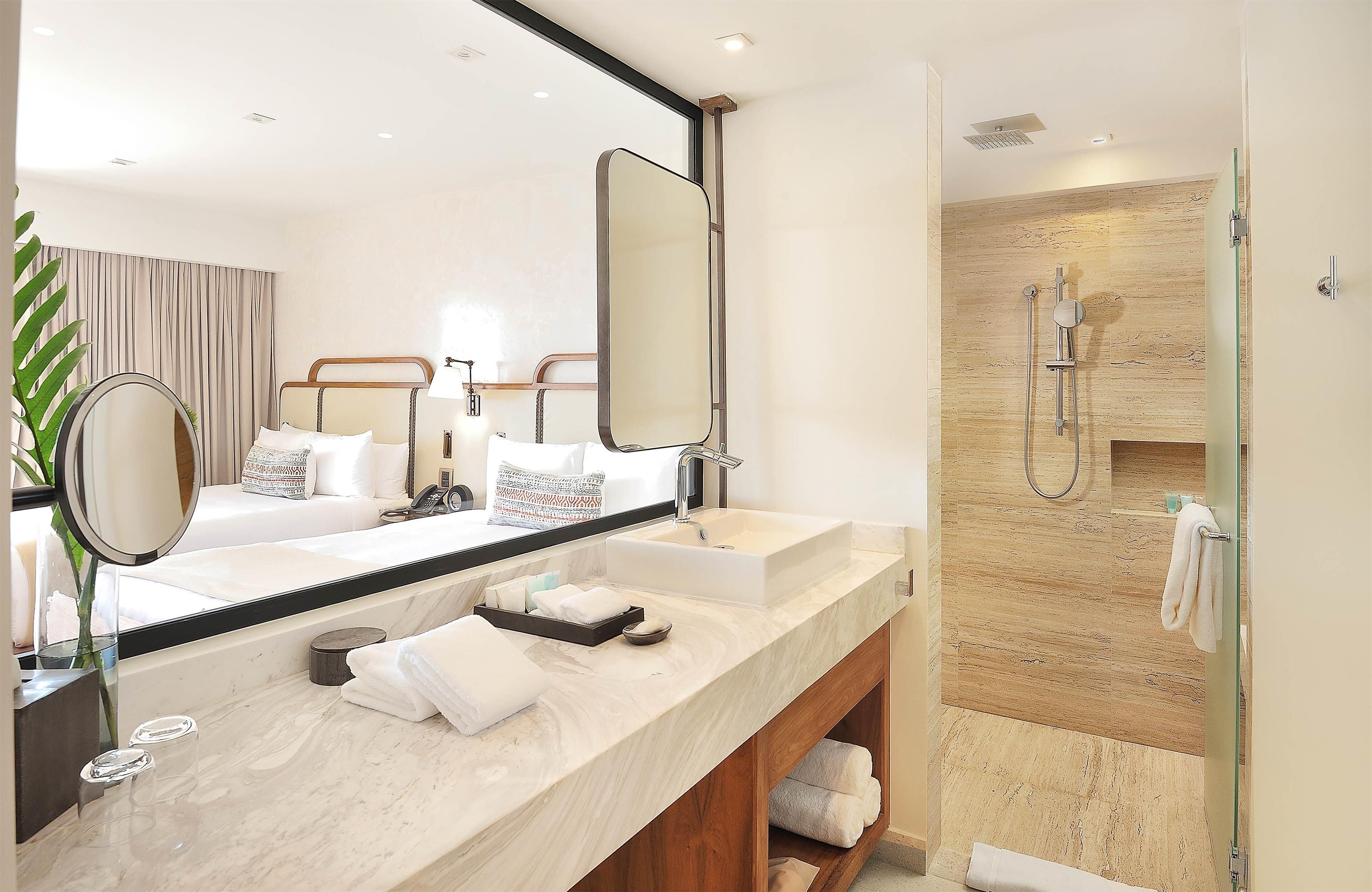 A modern bathroom with a large mirror, two sinks, a shower, and a vanity with towels.