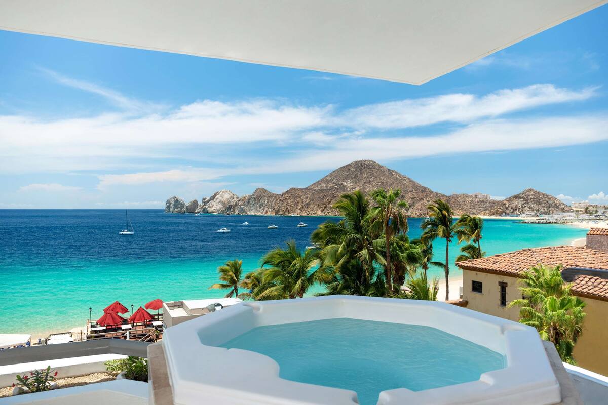 A rooftop pool with a view of the ocean, palm trees, and a mountain in the background.