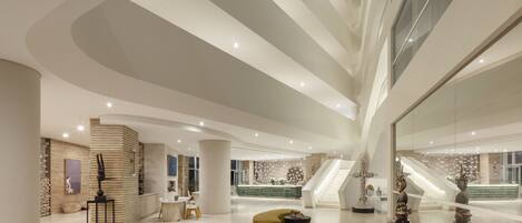 A spacious lobby with a curved seating area, a reception desk, and a staircase leading to an upper level.