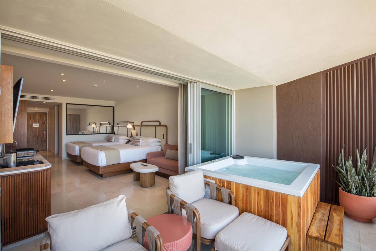 A hotel room with a large bed, a sitting area with a table, a hot tub, and a potted plant.