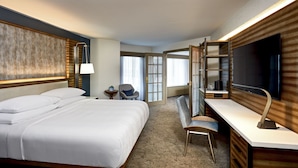 Une chambre d’hôtel avec un grand lit, un bureau avec une télévision, une chaise et une petite table avec une lampe.