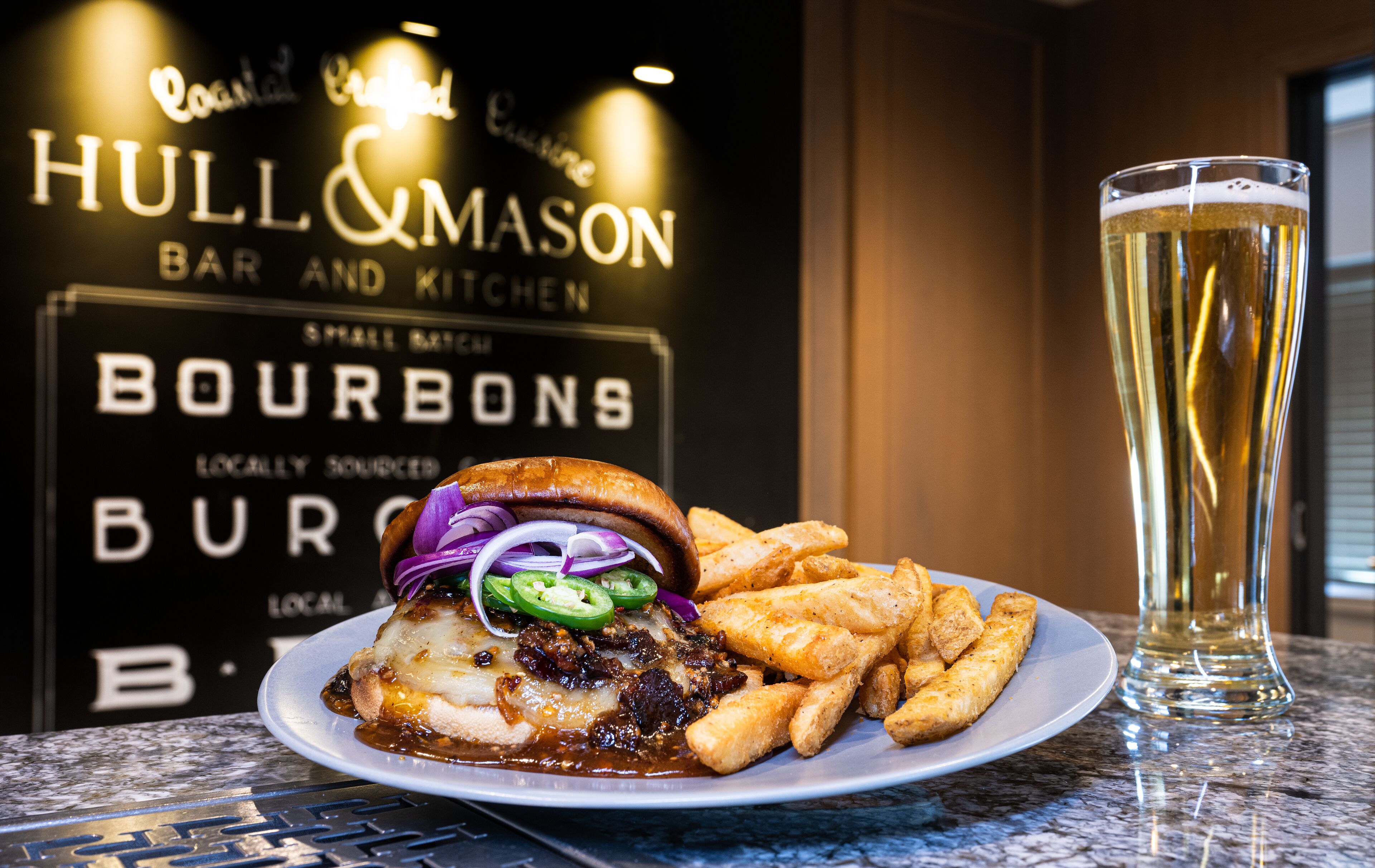 A plate of food with a burger and fries, a glass of beer, and a sign for 'Hull & Mason Bar and Kitchen'.