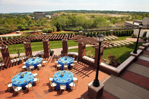 A patio area with multiple round tables and chairs, surrounded by brick pillars and a pergola.