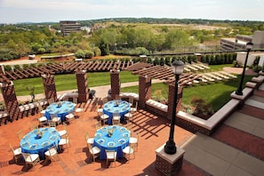 A patio area with multiple round tables and chairs, surrounded by brick pillars and a pergola.
