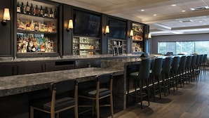 Un espace bar doté d’un long comptoir, de plusieurs étagères remplies de bouteilles et de tabourets de bar.