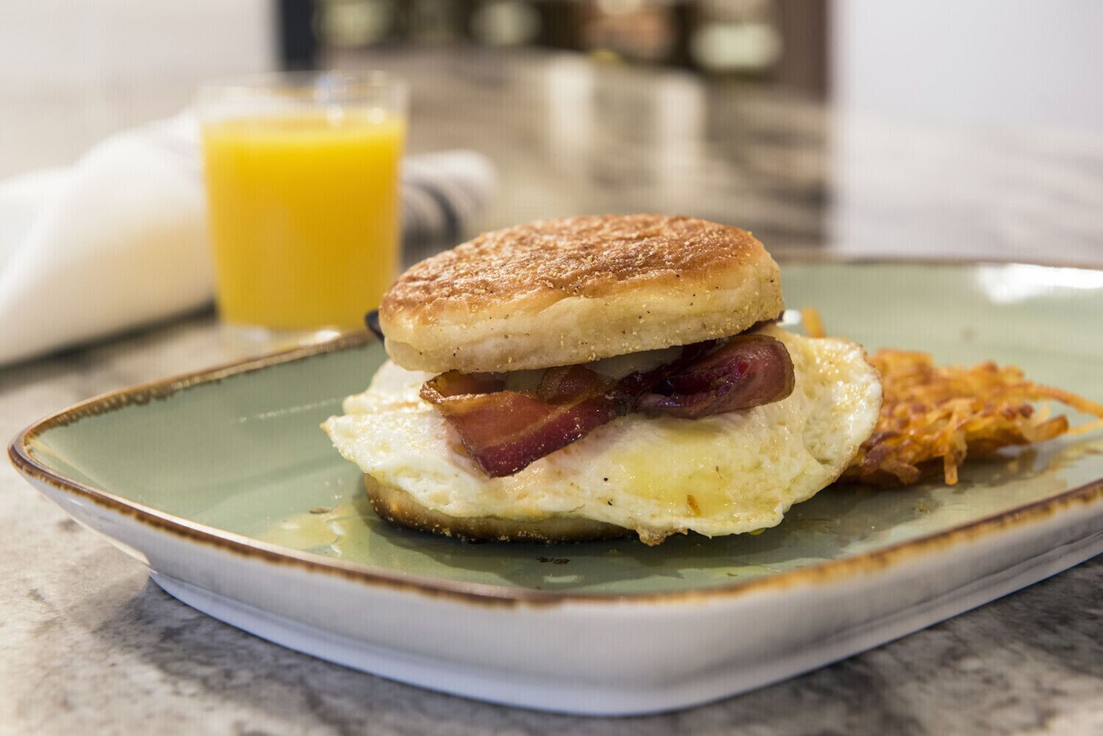 A breakfast plate with an egg sandwich, bacon, and hash browns on a ceramic plate.