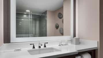 A modern bathroom with a large mirror, a sink with two faucets, and a glass shower enclosure.