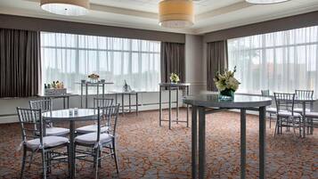 A conference room with round tables and chairs, large windows with curtains, and a patterned carpet.