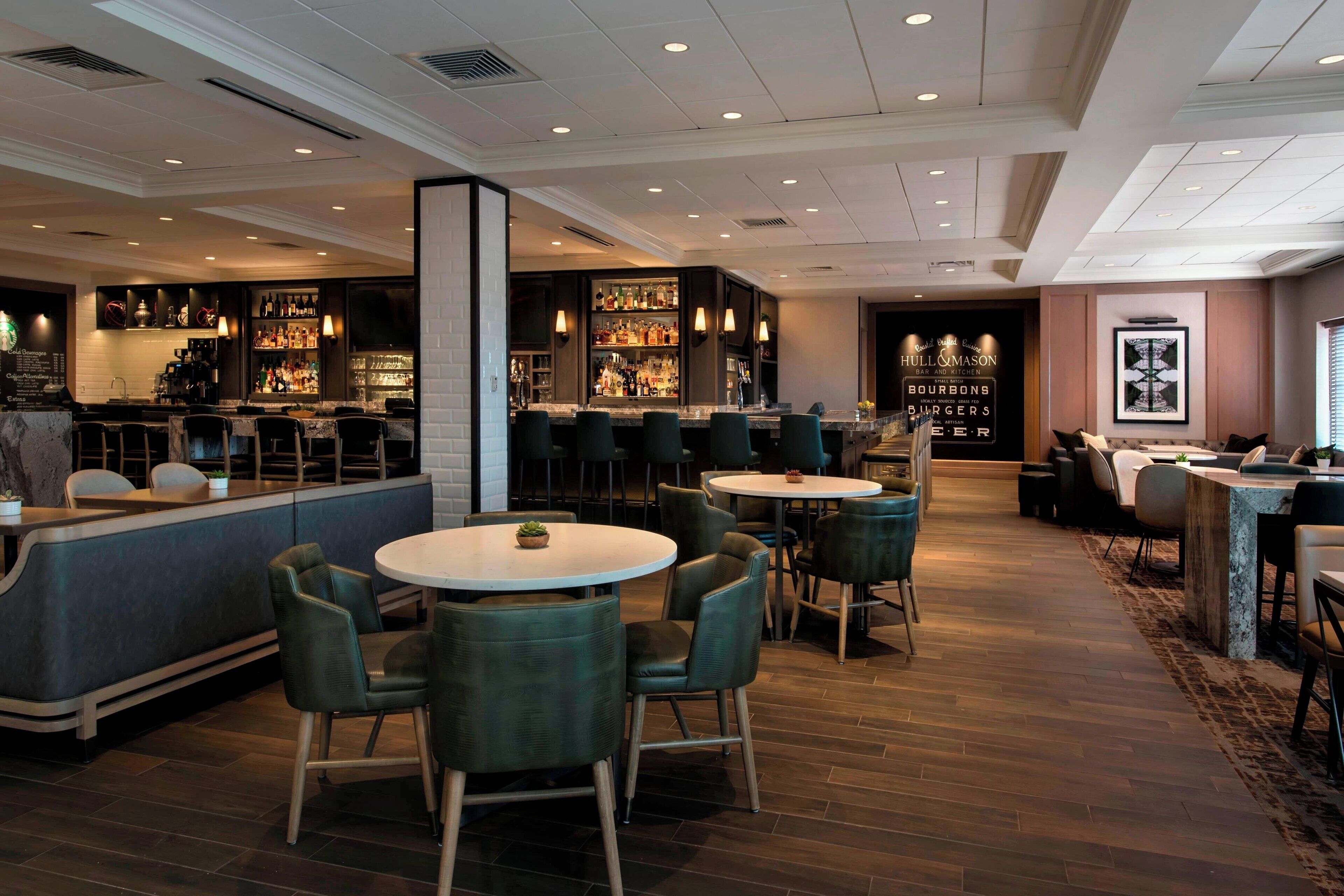 A modern bar area with seating and a bar counter, featuring a variety of liquor bottles and a menu board.