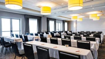 A conference room with rows of tables and chairs, large windows, and yellow hanging lamps.