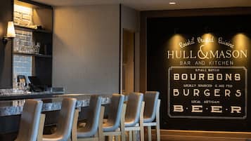 Angolo bar con un cartello che indica 'Hull & Mason Bar and Kitchen', che evidenzia proposte come bourbon, hamburger e birra.