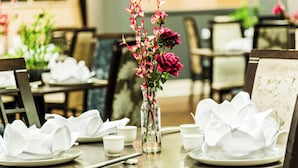 Una mesa de comedor con servilletas blancas, un jarrón con flores rosadas y una copa de vidrio.