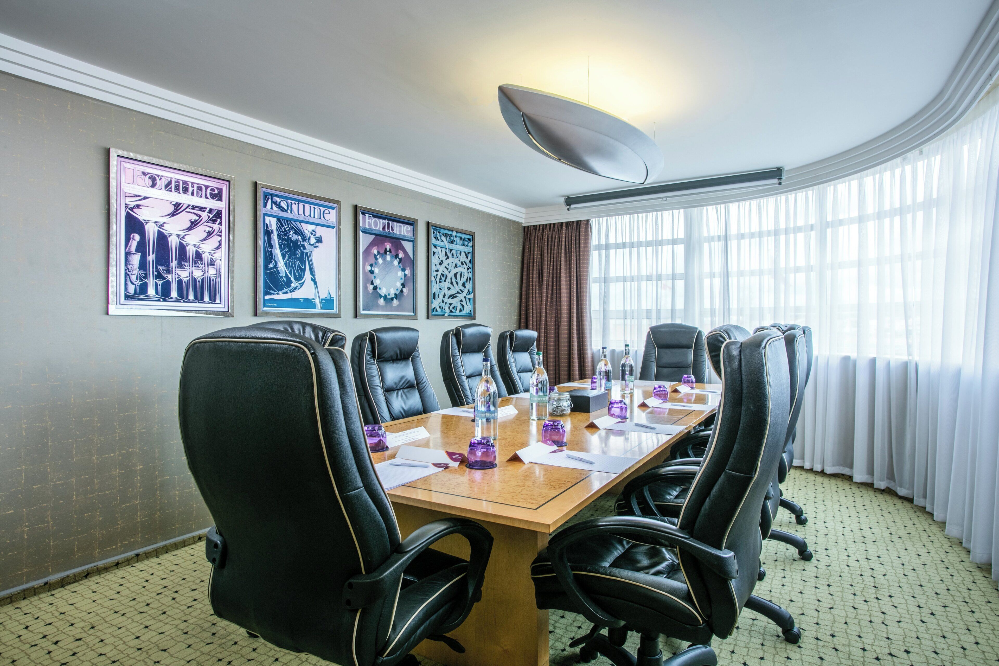 A conference room with a long table, black leather chairs, and framed posters on the wall.