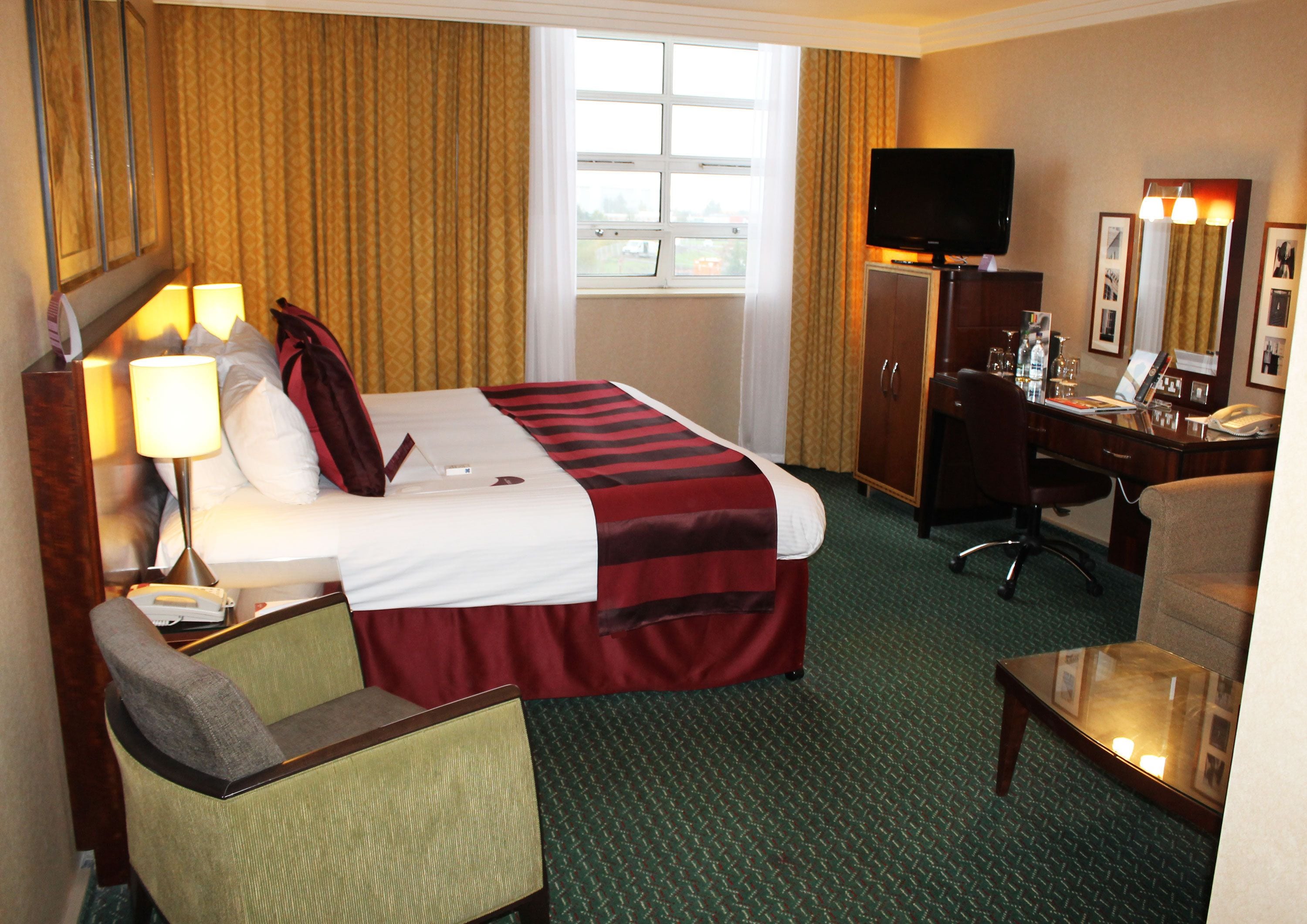 Una habitación de hotel con cama, escritorio, silla, televisor y ventana con cortinas.