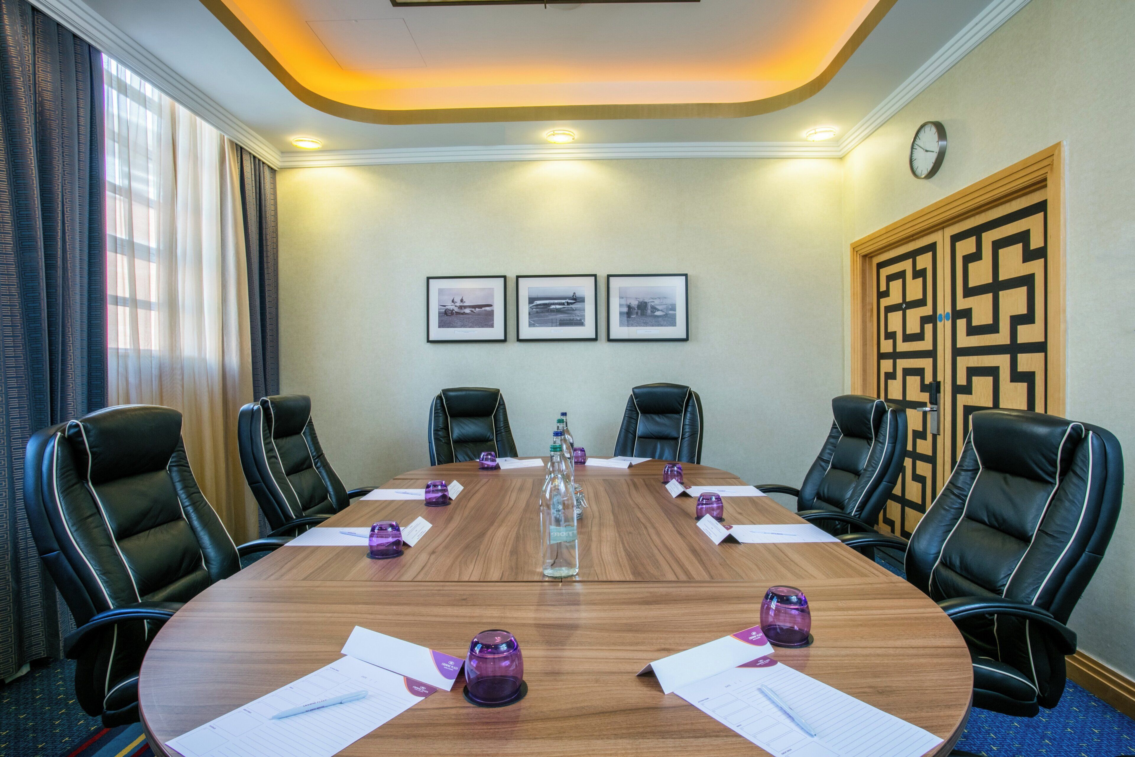 Un salón de conferencias con una mesa redonda, seis sillas de cuero negro, cuadros en la pared y un reloj.