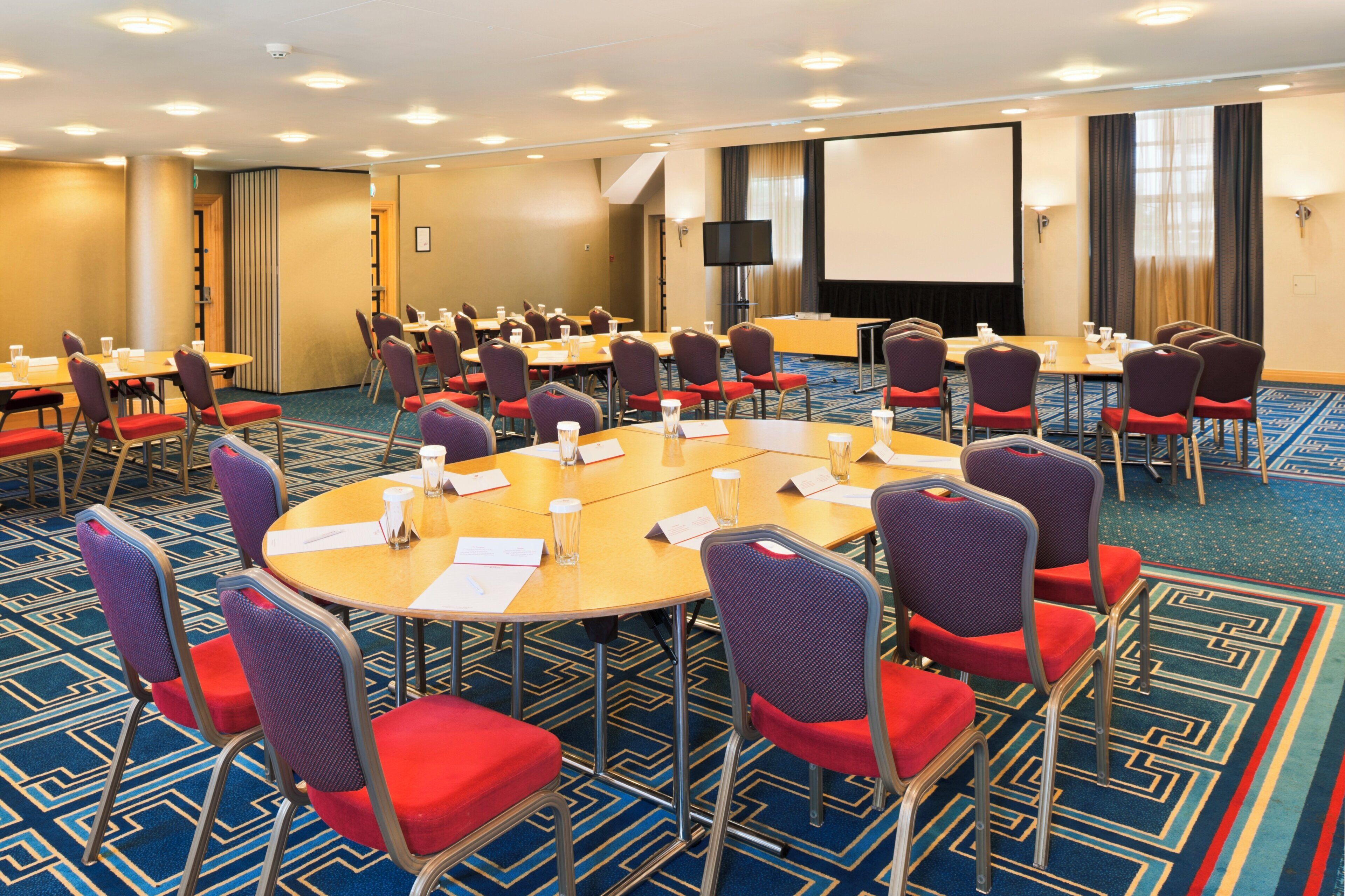 A conference room with round tables, chairs, and a projector screen.
