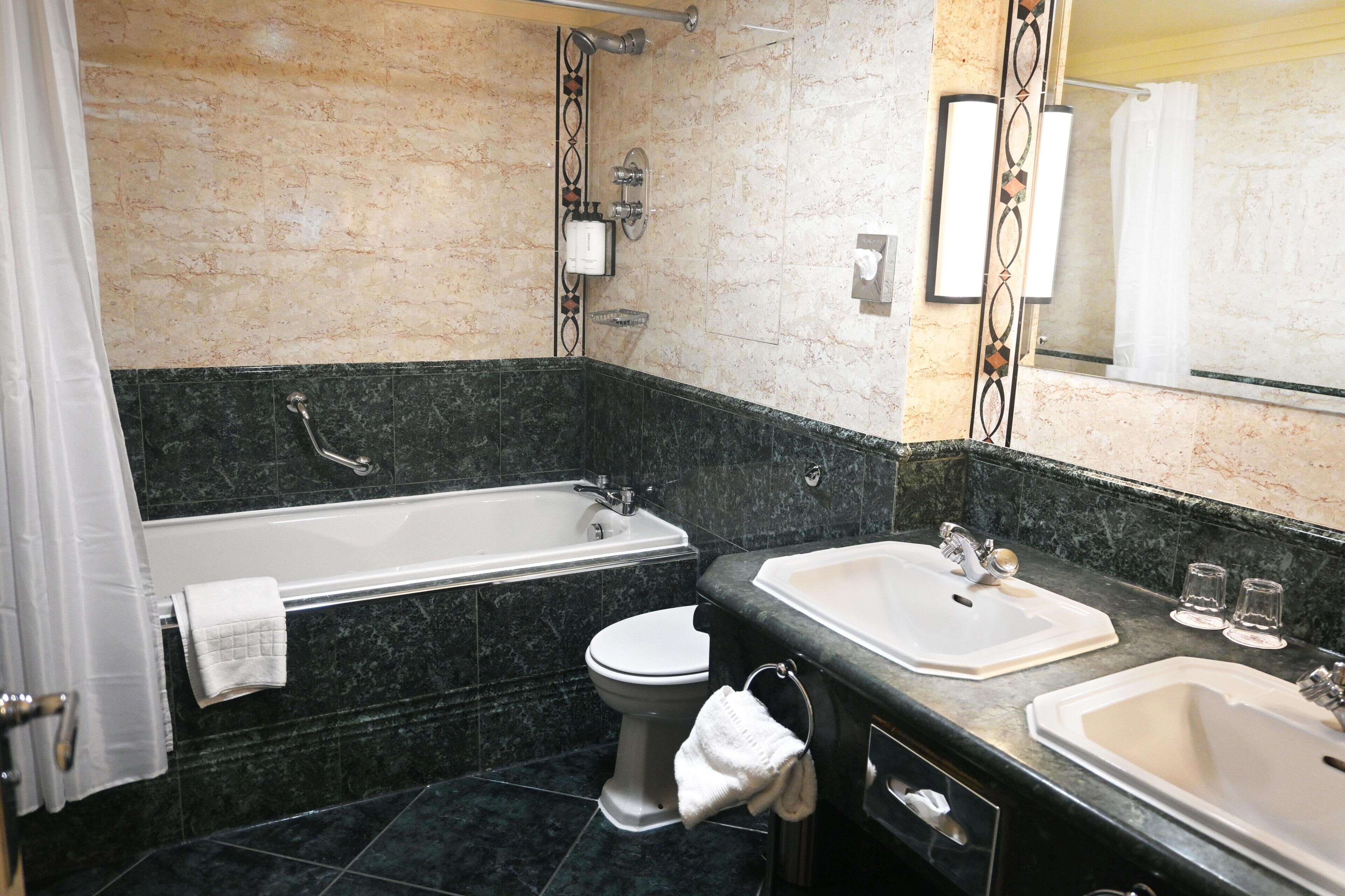 Un baño con bañera, dos lavamanos, un inodoro y un espejo.