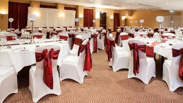 Un salón de banquetes con mesas redondas, manteles blancos y sillas con cintas rojas.