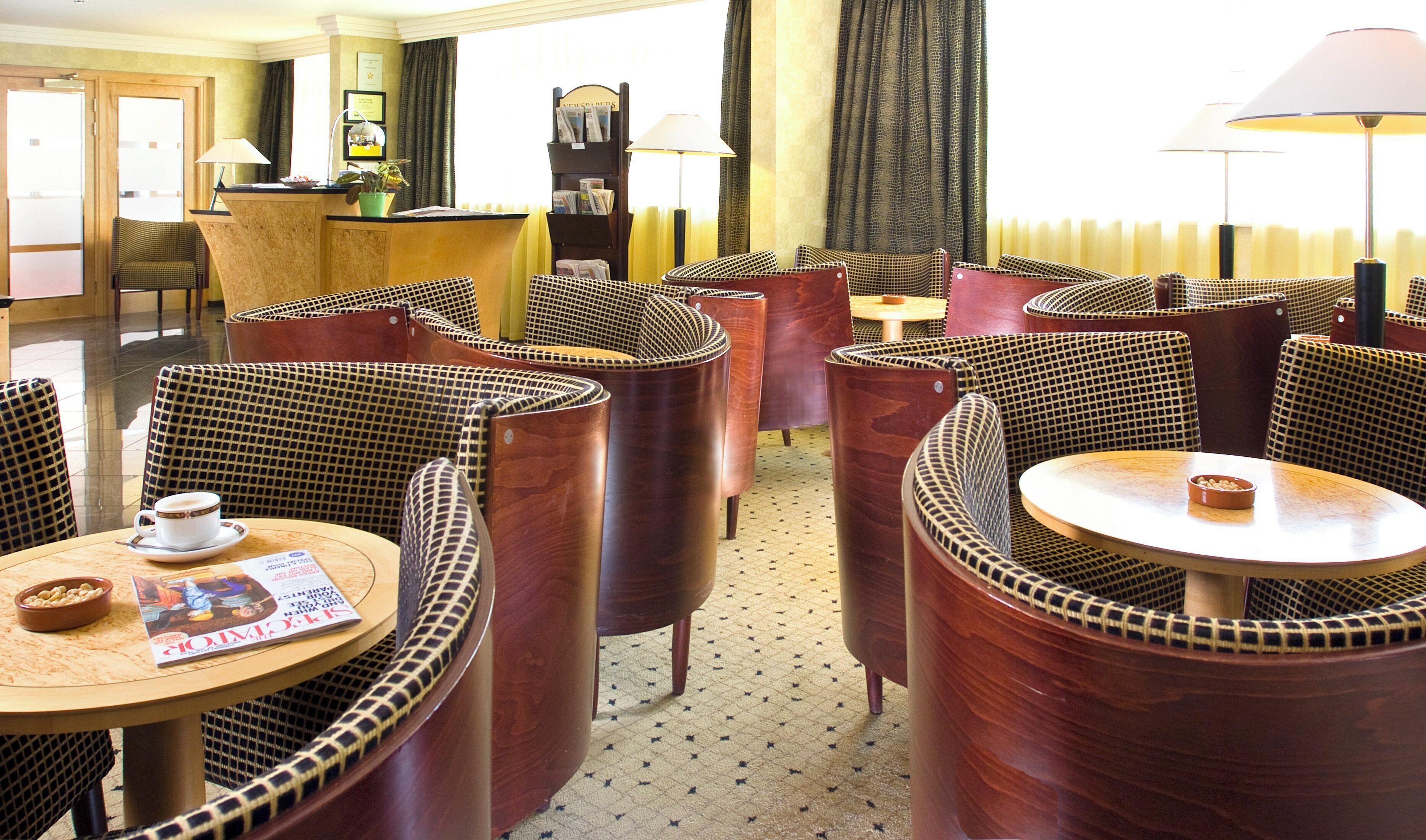 A hotel lobby with round tables, cushioned chairs, a reception desk, and a magazine on one of the tables.
