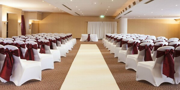 A hotel room with a long white carpet aisle, white chairs with red sashes, and beige walls.