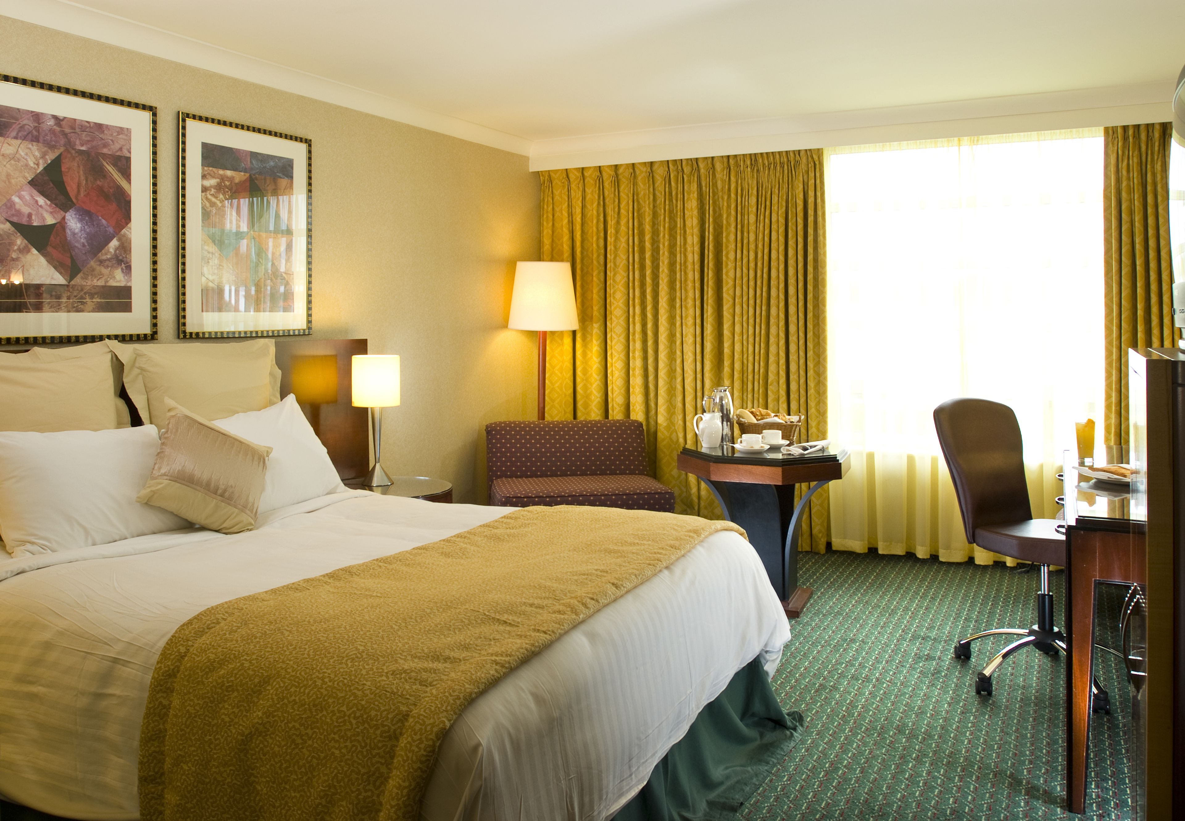 Une chambre d’hôtel avec un grand lit, un bureau avec une chaise, une lampe et une fenêtre avec des rideaux.