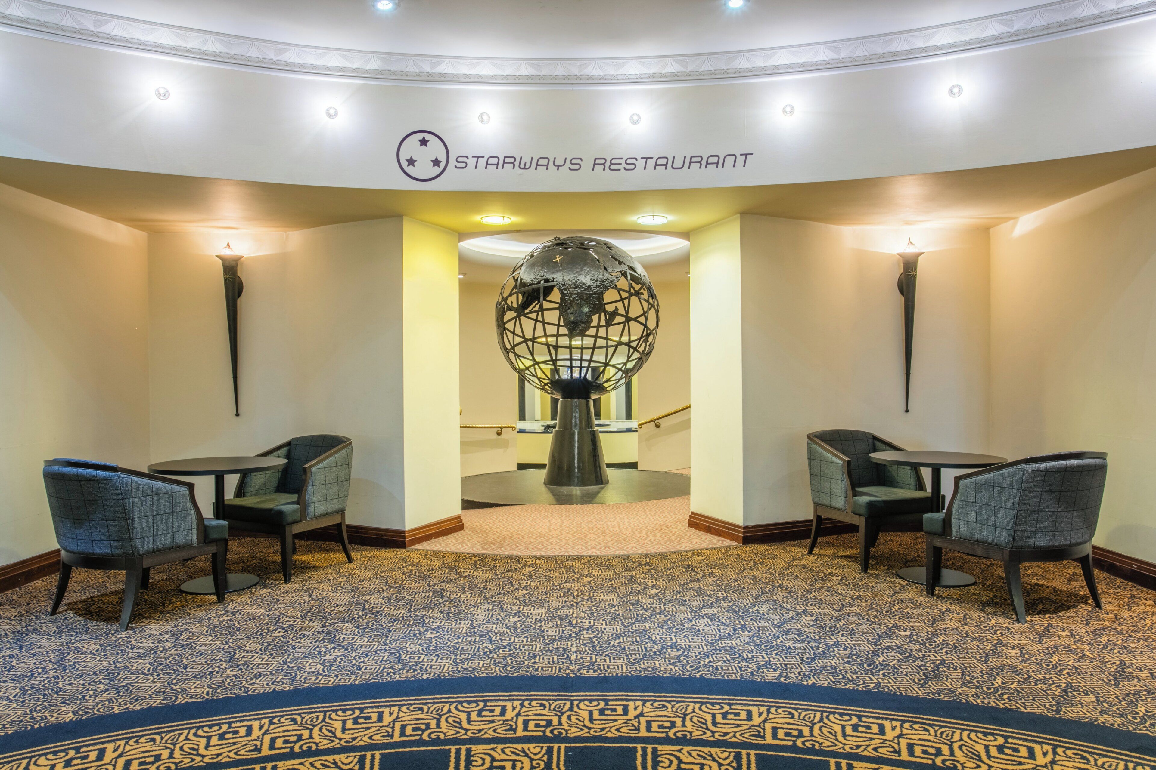 A Starways Restaurant with a modern interior, featuring a patterned carpet, two seating areas with chairs, and a decorative globe sculpture.