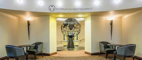 A Starways Restaurant with a modern interior, featuring a patterned carpet, two seating areas with chairs, and a decorative globe sculpture.