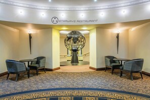 A Starways Restaurant with a modern interior, featuring a patterned carpet, two seating areas with chairs, and a decorative globe sculpture.
