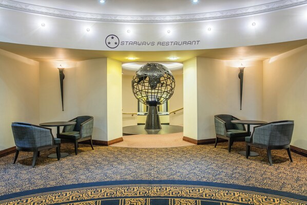A Starways Restaurant with a modern interior, featuring a patterned carpet, two seating areas with chairs, and a decorative globe sculpture.