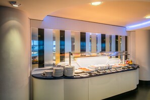 Ein reichhaltiges Buffet mit verschiedenen Speisen und Beilagen, eine Glaskabine und ein modernes Design mit Streifenpaneelen.