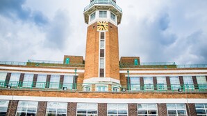 A brick tower with a clock, multiple windows, and a green railing.