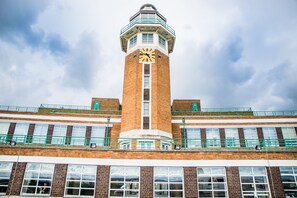 Une tour en briques surmontée d’une horloge, dotée de nombreuses fenêtres et d’un garde-corps vert.