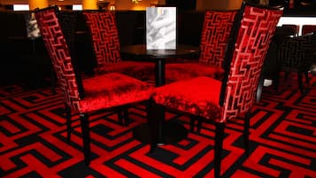 Un espace détente avec des fauteuils à revêtement rouge et une table, agrémenté d’un tapis à motifs géométriques.