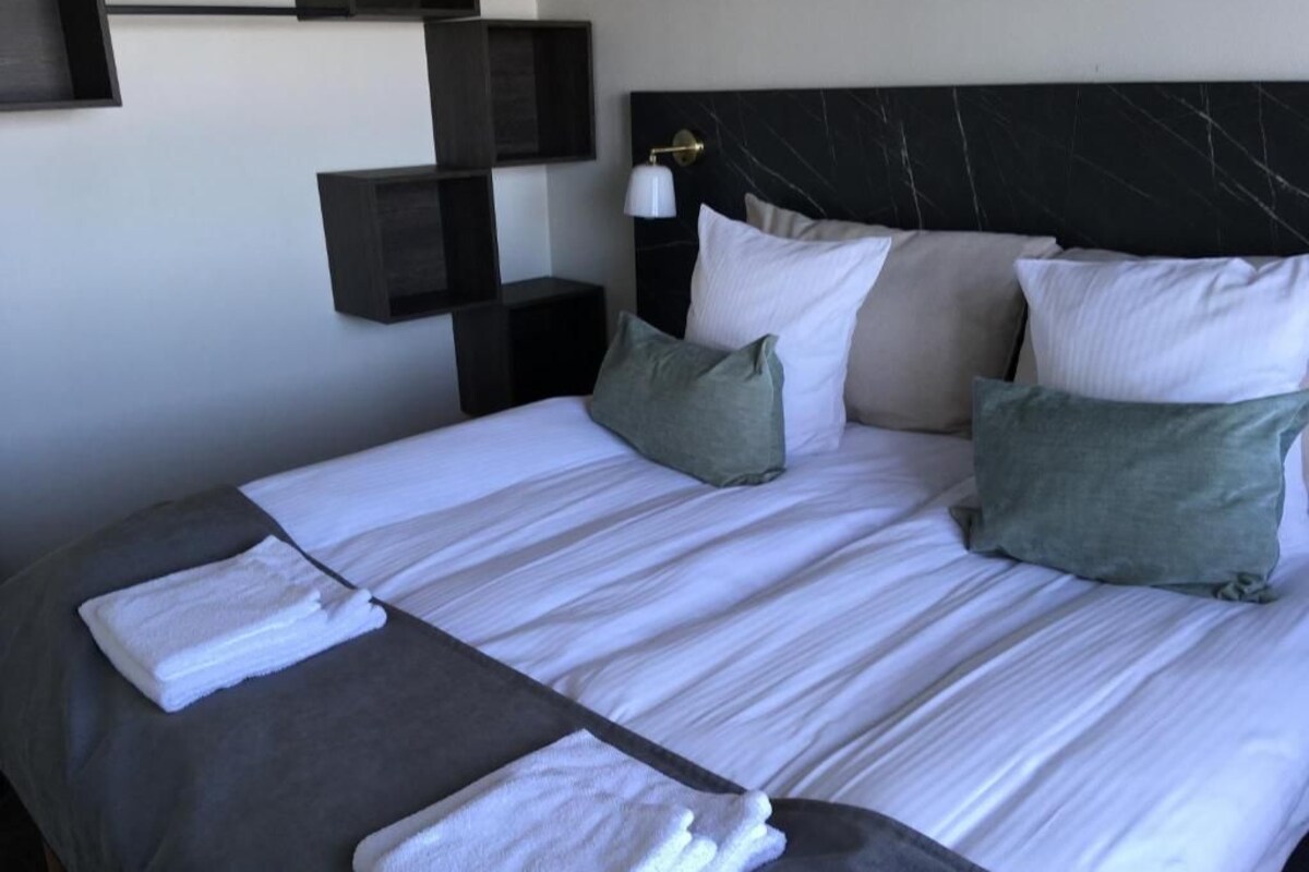 A neatly made bed with white linens, grey and green pillows, and a black headboard.