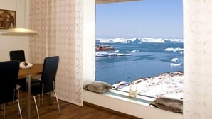 Ein Zimmer mit Essbereich, einem großen Fenster mit Blick auf Eisberge und Boote sowie einem Gemälde an der Wand.