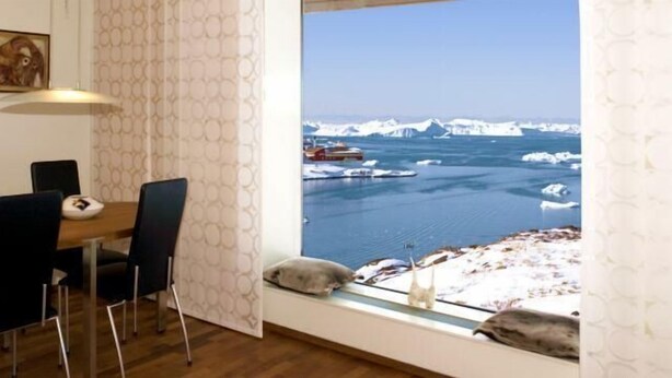 A room with a dining area, a large window with a view of icebergs and boats, and a painting on the wall. - Hotel Arctic (Ilulissat)