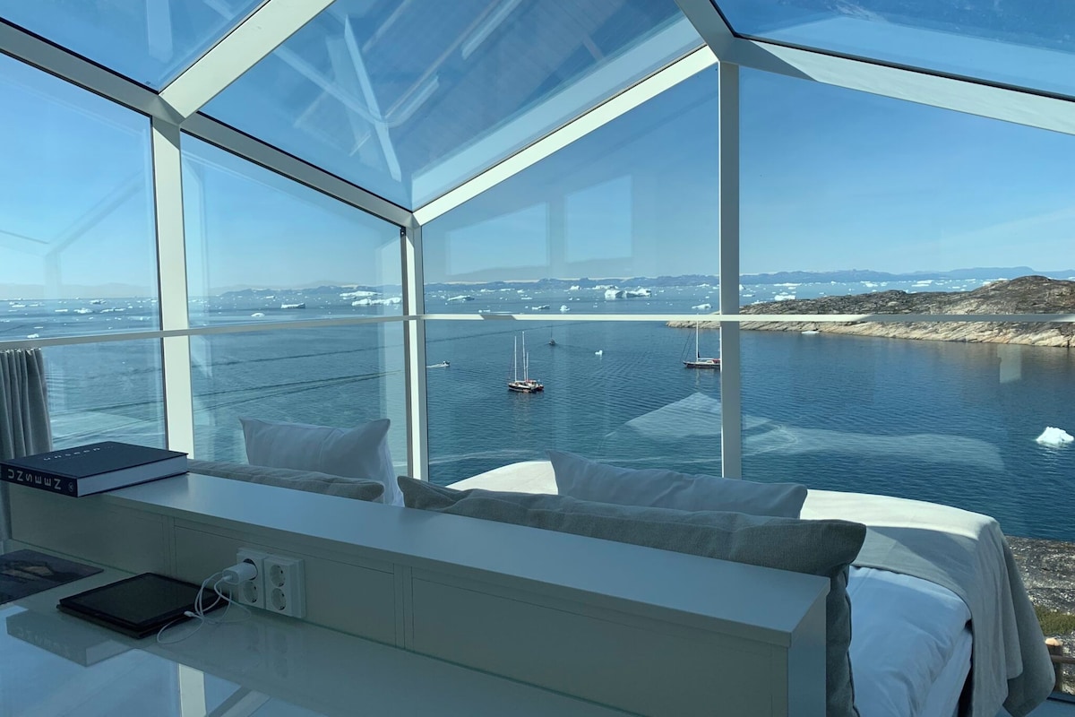 A modern room with a large glass window offering a view of a harbor with boats and icebergs.