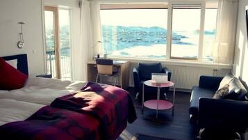 Habitación de hotel con cama, escritorio, silla y sofá. Se ve la playa a través de la ventana.
