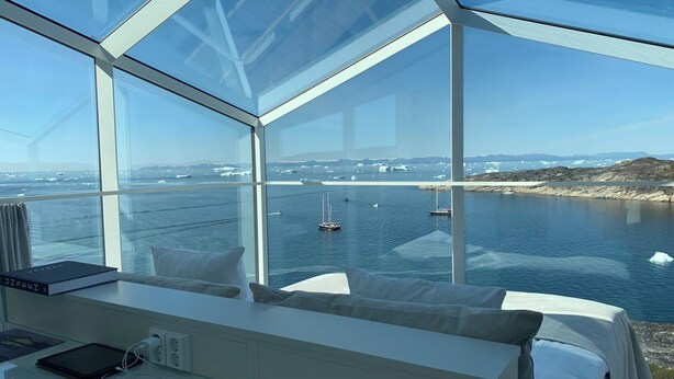 Ein modernes Zimmer mit einem großen Glasfenster und Blick auf einen Hafen mit Booten und Eisbergen.