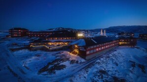 A hotel with multiple buildings, including a prominent red building with the name "HOTEL RICHTIC" visible. There are several smaller structures around, and the area is covered in snow. - Hotel Arctic (Ilulissat)