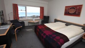 A hotel room with a bed, a desk, a chair, a small table, and a window with a view of the sea. - Hotel Arctic (Ilulissat)