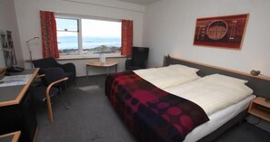 Habitación de hotel con cama, escritorio, silla, una mesita y ventana con vista al mar.