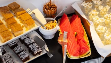 Ein Buffet mit verschiedenen Speisen, darunter Brownies, eine Schüssel mit Nüssen, Wassermelonenstücke und Popcorn.