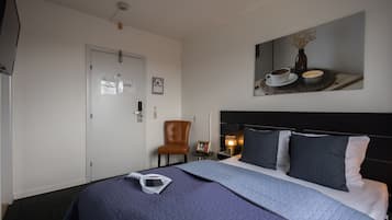 A hotel room with a bed, a chair, a bedside table with a lamp, and a wall-mounted artwork.