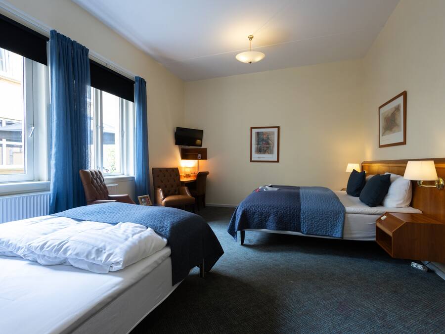 A hotel room with two beds, a desk, a chair, a TV, and a framed picture on the wall.