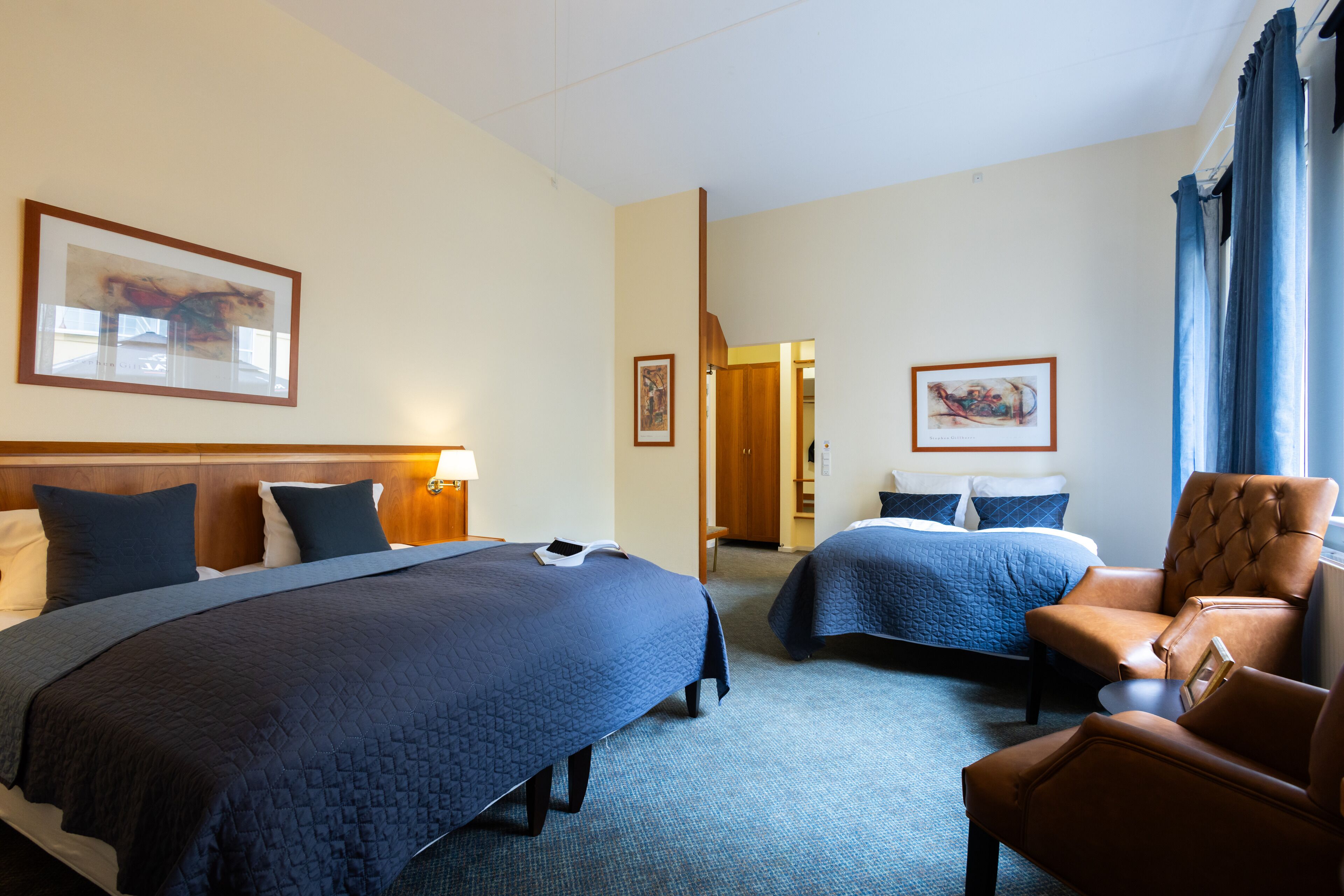 A hotel room with two beds, a sitting area with a chair, and artwork on the walls.